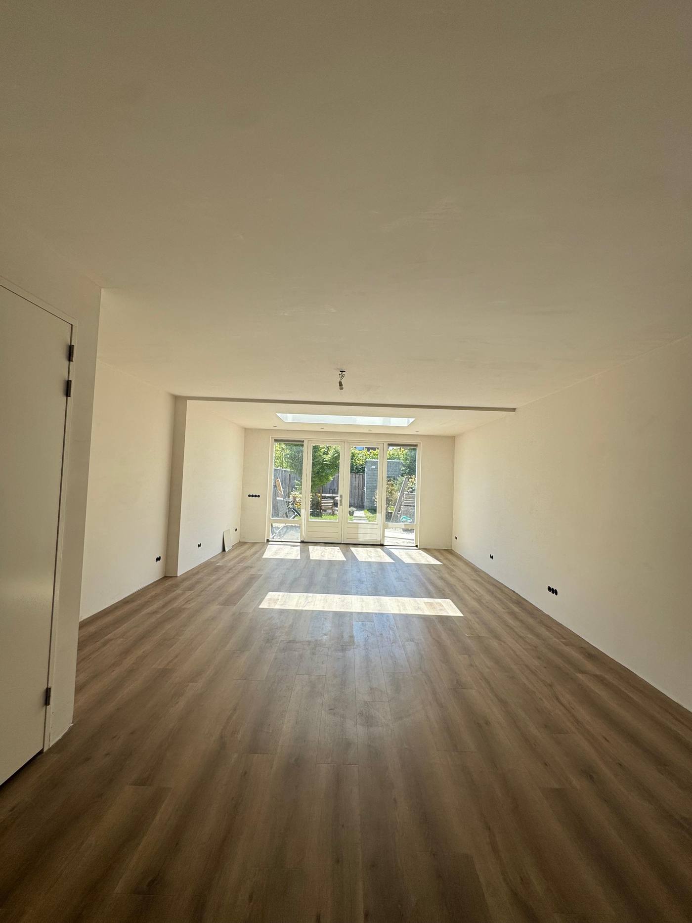 De afgewerkte aanbouw vanbinnen, met doorgelegde vloer, lichtstraat in het plafond en zicht op de tuin