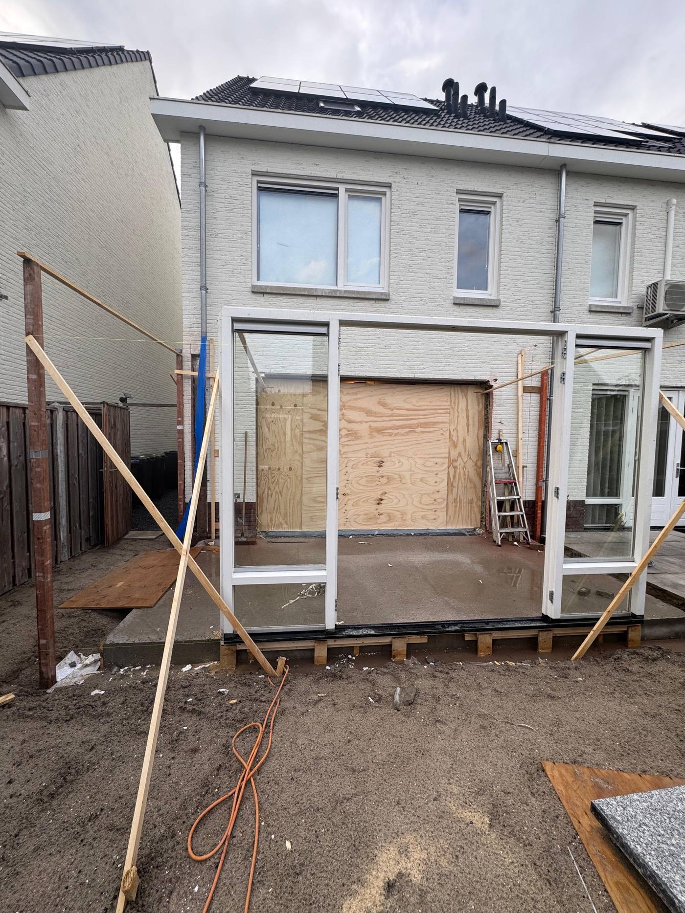 Het bestaande kozijn herplaatst in de nieuwe achtergevel tijdens de bouw, met tijdelijke beplating en steigerwerk