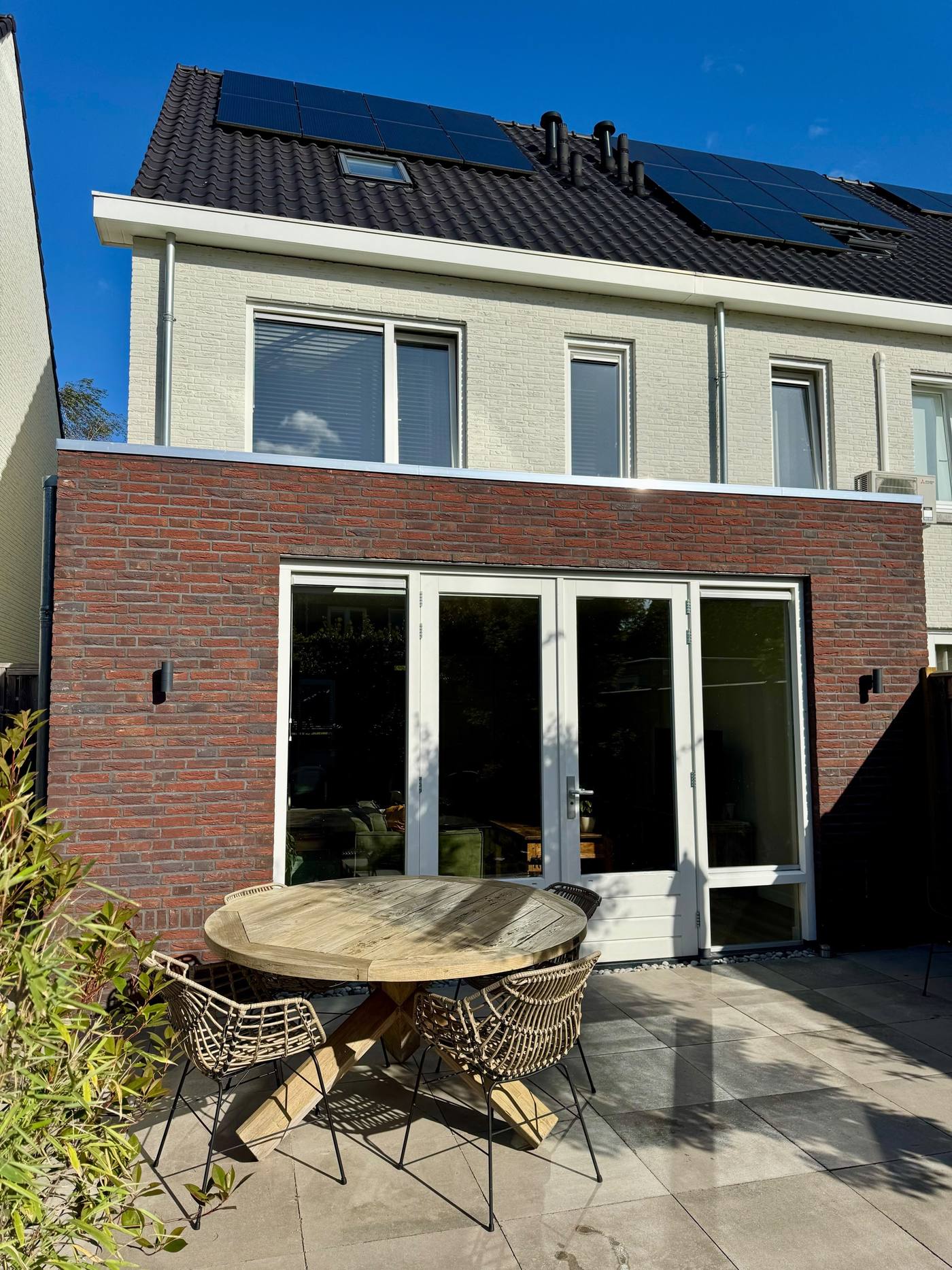 De afgeronde aanbouw gezien vanuit de tuin, met het herplaatste kozijn en nieuw terras